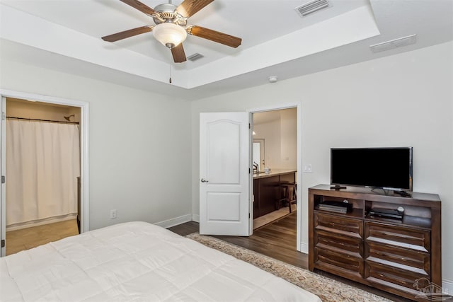 bedroom with a tray ceiling, connected bathroom, ceiling fan, and wood-type flooring