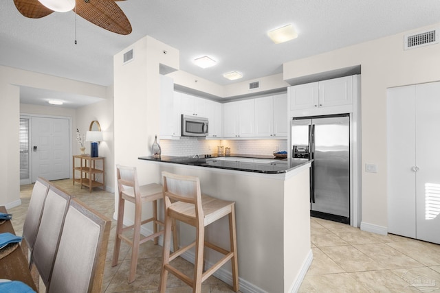 kitchen featuring kitchen peninsula, tasteful backsplash, stainless steel appliances, ceiling fan, and white cabinetry