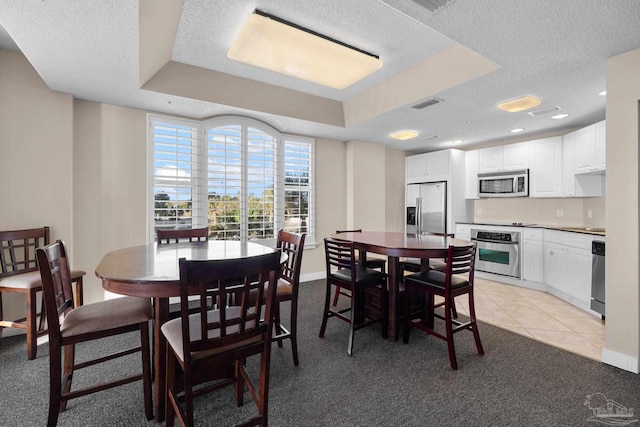 dining area with light tile patterned floors, a textured ceiling, and a tray ceiling