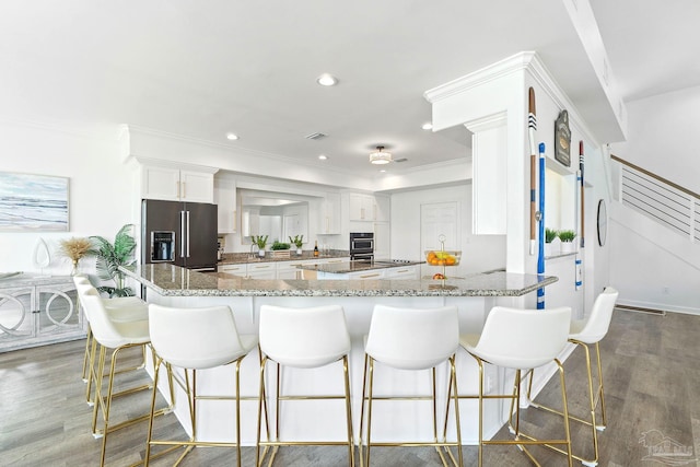 kitchen with high quality fridge, black oven, light stone counters, and kitchen peninsula