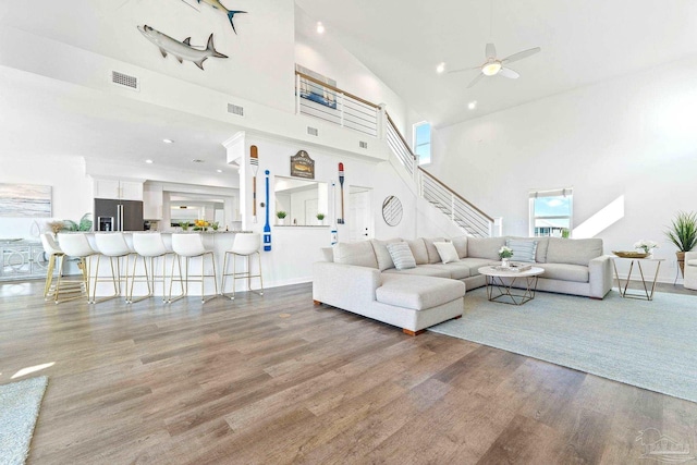 living room with hardwood / wood-style flooring, a towering ceiling, and ceiling fan