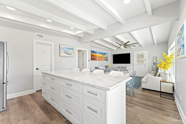 kitchen with stainless steel fridge, white cabinetry, a center island, light stone countertops, and lofted ceiling with beams