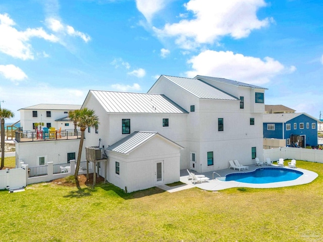 rear view of house featuring a fenced in pool, a balcony, and a lawn