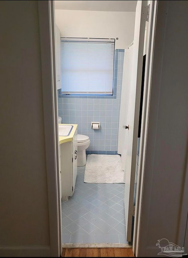 bathroom with tile walls, walk in shower, tile patterned floors, vanity, and toilet