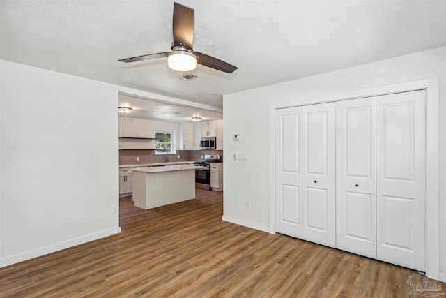 kitchen with a kitchen island, a textured ceiling, white cabinetry, light wood-type flooring, and stainless steel appliances