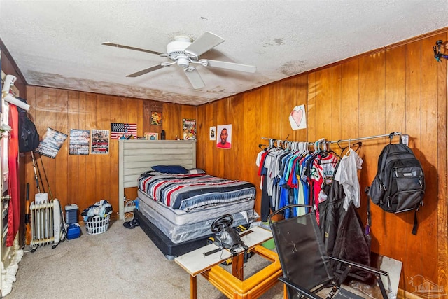 bedroom featuring ceiling fan, wooden walls, light carpet, and a textured ceiling