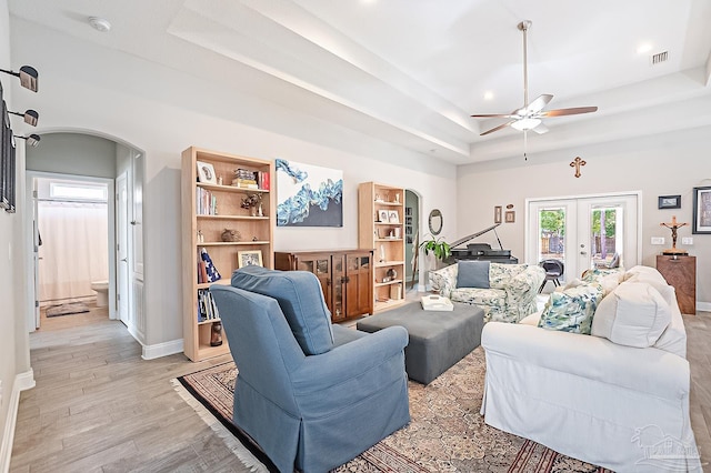 living room with a tray ceiling, light hardwood / wood-style floors, french doors, and ceiling fan