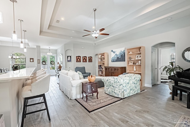 living room featuring a tray ceiling, french doors, ceiling fan, and light wood-type flooring