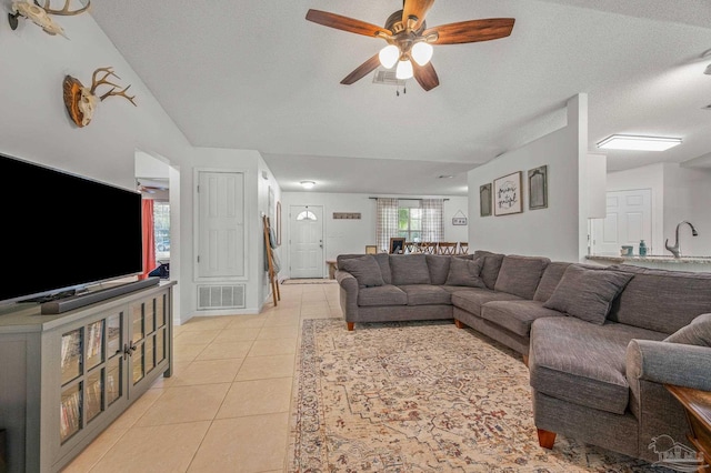 living room with vaulted ceiling, light tile patterned floors, a textured ceiling, ceiling fan, and visible vents