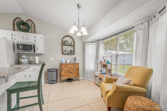 kitchen featuring vaulted ceiling, stainless steel microwave, a chandelier, light tile patterned floors, and white cabinets