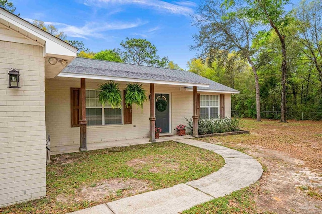 ranch-style home with covered porch, brick siding, and roof with shingles