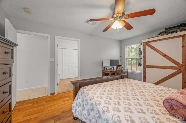 bedroom with light wood-type flooring, a textured ceiling, ceiling fan, and visible vents