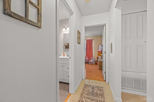 corridor featuring light tile patterned floors, a textured wall, baseboards, a textured ceiling, and a sink