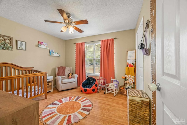 bedroom featuring a textured ceiling, wood finished floors, ceiling fan, and a nursery area