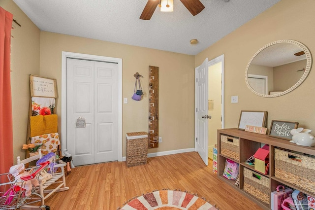 playroom with baseboards, a textured ceiling, wood finished floors, and a ceiling fan