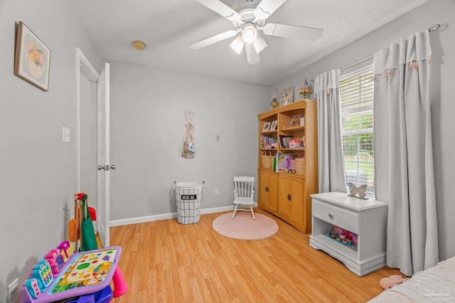 recreation room featuring baseboards, a ceiling fan, light wood-style floors, and a textured ceiling