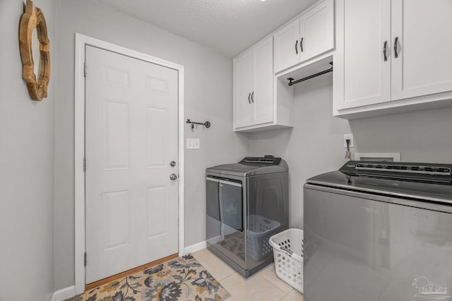 laundry room with light tile patterned flooring, a textured ceiling, baseboards, cabinet space, and washer and clothes dryer