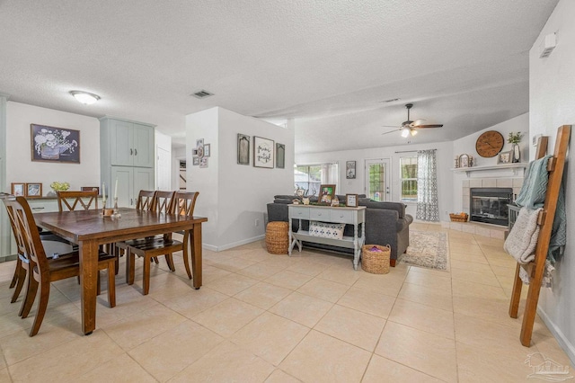 dining area with light tile patterned flooring, a textured ceiling, visible vents, a tile fireplace, and ceiling fan