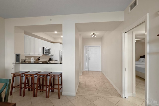 kitchen with kitchen peninsula, appliances with stainless steel finishes, a kitchen breakfast bar, white cabinetry, and light tile patterned flooring