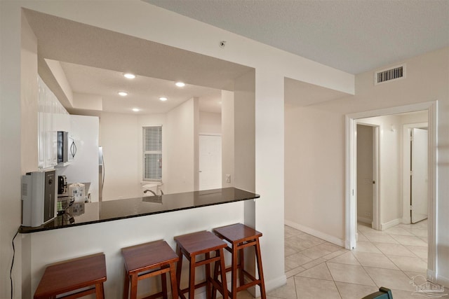 kitchen featuring kitchen peninsula, a textured ceiling, a kitchen bar, and light tile patterned flooring