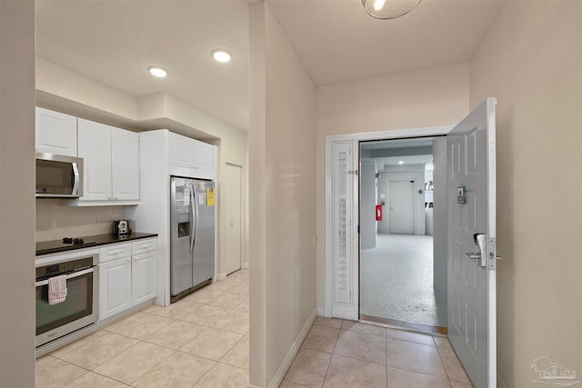 kitchen featuring light tile patterned floors, a textured ceiling, stainless steel appliances, and white cabinetry