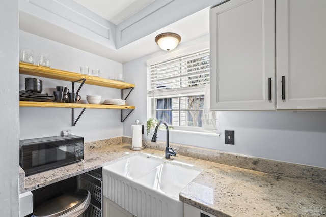 kitchen with black microwave, a sink, open shelves, and light stone countertops