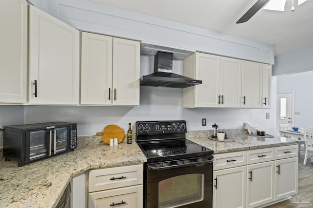 kitchen with light stone counters, black range with electric stovetop, white cabinetry, a ceiling fan, and wall chimney range hood