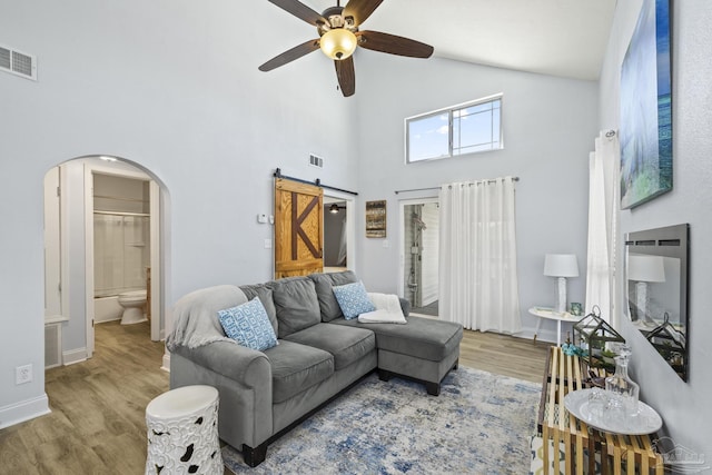 living room featuring arched walkways, a barn door, wood finished floors, and visible vents