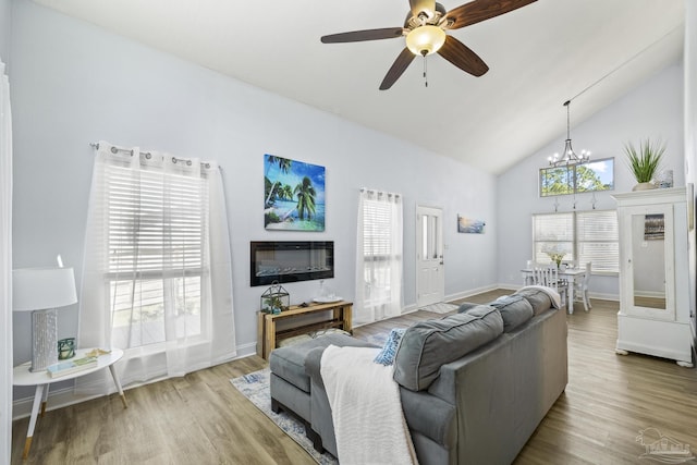 living room featuring ceiling fan with notable chandelier, high vaulted ceiling, wood finished floors, and baseboards