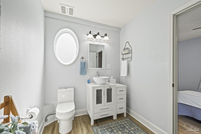 ensuite bathroom featuring connected bathroom, toilet, wood finished floors, visible vents, and baseboards