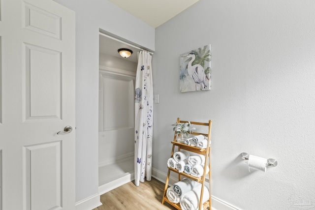 bathroom featuring baseboards, wood finished floors, and a shower with shower curtain