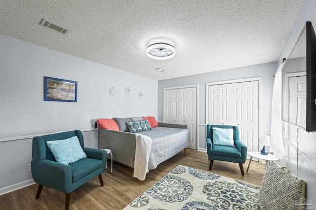 bedroom featuring wood finished floors, visible vents, baseboards, and two closets