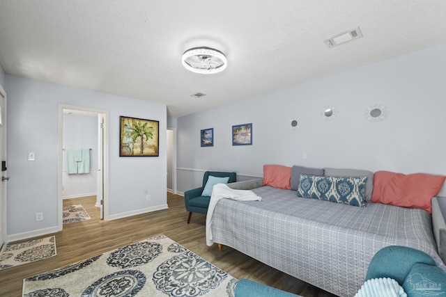 bedroom featuring a textured ceiling, wood finished floors, visible vents, and baseboards