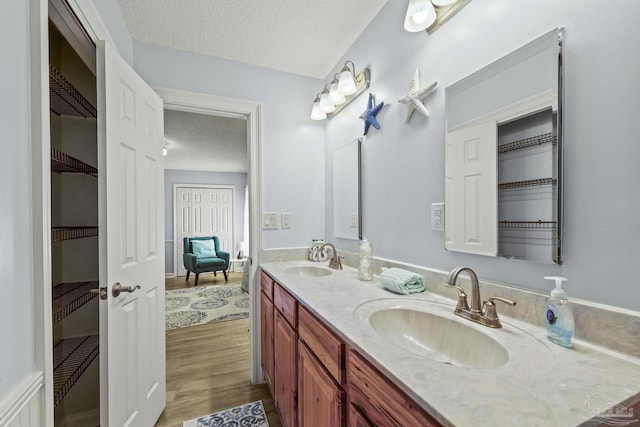 full bath with double vanity, a sink, a textured ceiling, and wood finished floors