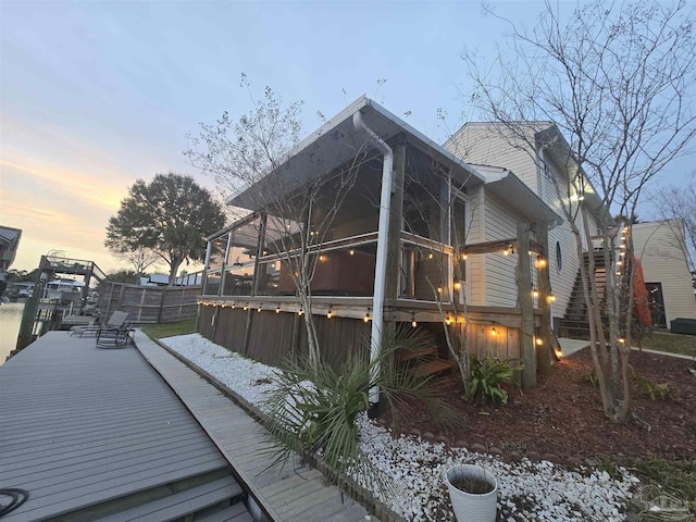 view of side of home featuring stairs, a deck, fence, and a sunroom