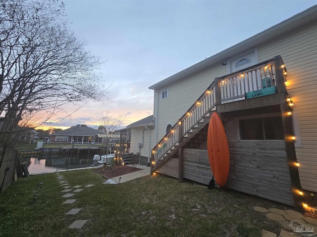 back of property at dusk featuring stairs, a deck, and a lawn