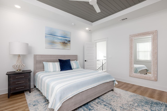 bedroom with light wood-type flooring, wood ceiling, a raised ceiling, ceiling fan, and crown molding