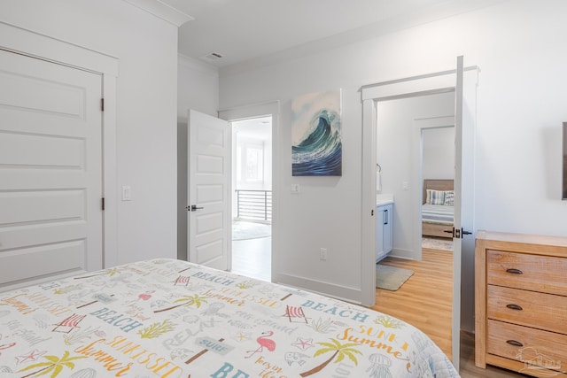 bedroom featuring wood-type flooring, ornamental molding, and ensuite bath