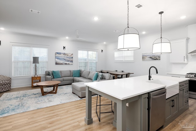 kitchen featuring sink, appliances with stainless steel finishes, a kitchen island with sink, white cabinets, and light wood-type flooring