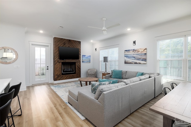 living room with a large fireplace, light hardwood / wood-style flooring, ceiling fan, and ornamental molding