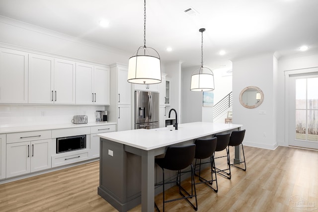 kitchen with stainless steel refrigerator with ice dispenser, backsplash, a kitchen island with sink, built in microwave, and white cabinetry