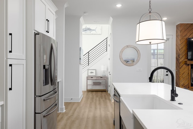 kitchen featuring ornamental molding, stainless steel appliances, sink, white cabinets, and hanging light fixtures