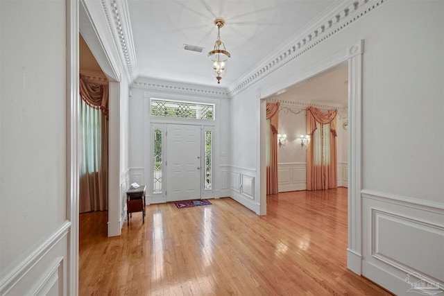 foyer with light wood-type flooring, crown molding, and a chandelier