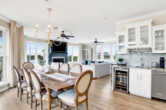 dining room featuring wine cooler, ceiling fan with notable chandelier, light hardwood / wood-style floors, crown molding, and wet bar