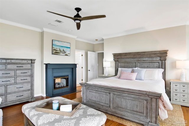 bedroom with a tiled fireplace, ornamental molding, ceiling fan, and dark hardwood / wood-style floors