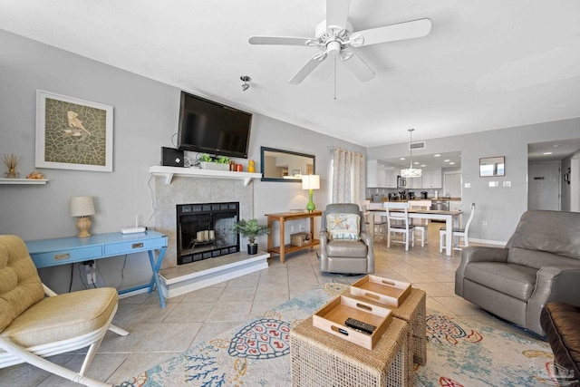 living room with light tile patterned floors, baseboards, a ceiling fan, and a tiled fireplace