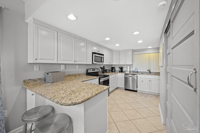 kitchen featuring a peninsula, recessed lighting, a sink, stainless steel appliances, and white cabinetry