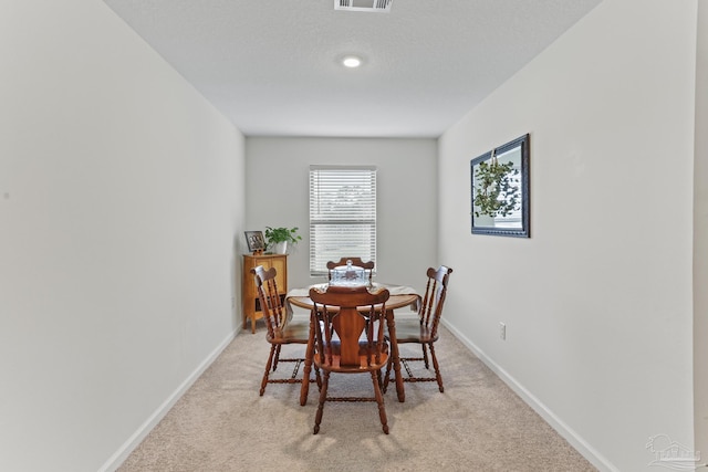 dining room featuring light colored carpet, visible vents, baseboards, and a textured ceiling