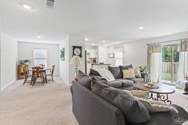 living room featuring light carpet, plenty of natural light, visible vents, and baseboards