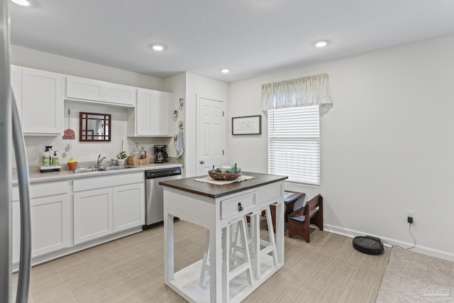 kitchen with recessed lighting, stainless steel dishwasher, white cabinetry, a sink, and baseboards